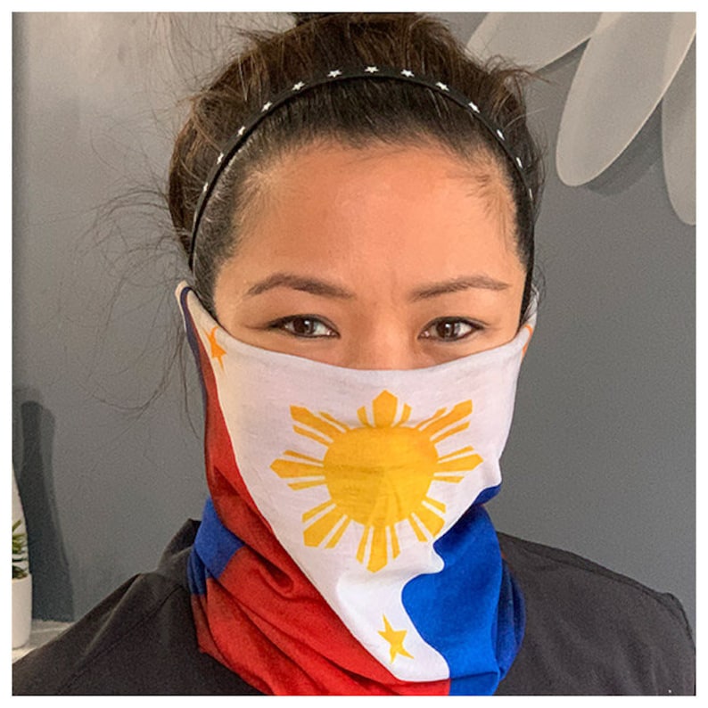 May include: A woman wearing a face covering with the Philippine flag printed on it. The flag is white with a yellow sun and eight rays, and a blue triangle with a white star at the bottom.