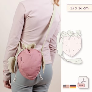 May include: A strawberry-shaped drawstring bag in dusty pink with light green leaf accents and a long shoulder strap. The bag features small embroidered dots and measures 13 x 16 cm. A digital PDF pattern illustration is included in the image.