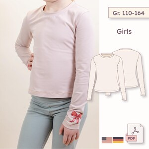 Könnte beinhalten: Hellrosa Langarmshirt mit Rundhalsausschnitt. Am Ärmelaufschlag befindet sich ein rotes Schleifendesign. Das Bild enthält auch eine Strichzeichnung des Shirts und den Text "Girls" und "Gr. 110-164".