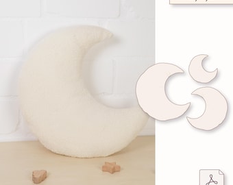 May include: A cream-colored, crescent moon-shaped pillow made of a soft, textured fabric. The pillow is next to three crescent moon templates in different sizes. The text "S,M,L" is above the templates.