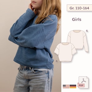 Könnte beinhalten: Ein blaues Langarmshirt mit strukturierter Oberfläche, kombiniert mit einer hellblauen Jeans. Das Bild enthält eine technische Schnittmuster-Illustration für ein Oberteil mit kurzen oder langen Ärmeln, beschriftet mit Gr. 110-164, Girls, und ein PDF-Symbol.