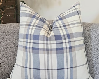Könnte beinhalten: Ein quadratisches Dekokissen mit einem Karomuster in Blau-, Weiß- und Grautönen. Der Stoff zeigt ein klassisches, sich überschneidendes Gitterdesign mit unterschiedlich dicken Linien, das eine ausgewogene geometrische Anordnung bildet.