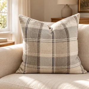 May include: A square throw cushion featuring a plaid pattern in shades of grey, beige, and white. The fabric has a visible woven texture, and the design consists of intersecting horizontal and vertical lines forming a classic grid motif.