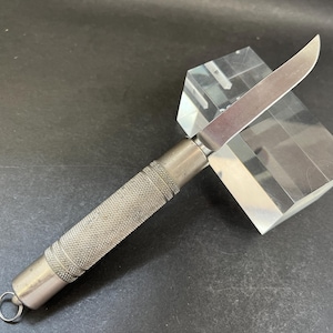 May include: A silver pocket knife with a textured handle and a sharp blade. The knife is displayed on a clear acrylic block.