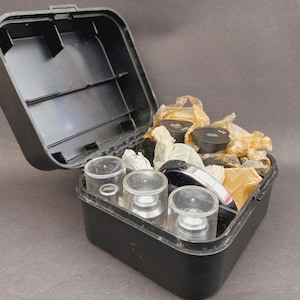 May include: A white ceramic mug with a black handle and the text "But First, Coffee" in a black, bold font. The mug is on a white surface.