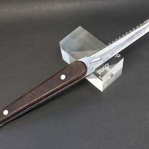 May include: A brown handled saw knife with a serrated blade. The blade is marked with the text "UOCO."