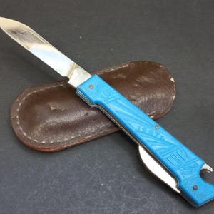 Può includere: Un coltellino tascabile blu con una lama argentata e un apribottiglie. Il coltellino ha un fodero in pelle e le parole "1917" e "URSS" sono incise sul manico.