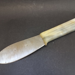 May include: A vintage knife with a metal blade and a white plastic handle. The handle has a textured design.