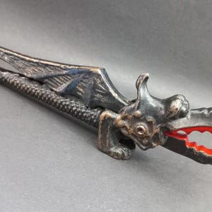 May include: A black cast iron dragon nutcracker with red painted teeth. The dragon has wings and a textured body.