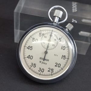 May include: A silver Sekonda stopwatch with a white face and black markings. The stopwatch has a 1/5 second scale and a 60-second dial. It is a 16-jewel watch.