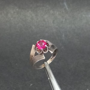 May include: A silver ring with a pink gemstone set in a flower-shaped design.