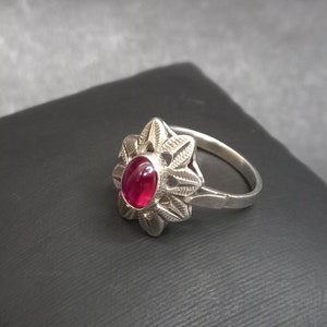 Può includere: Un anello d'argento con una pietra preziosa rossa incastonata in un design floreale.