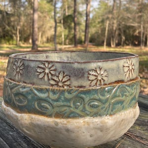 Peut inclure: Ensemble de trois mugs en céramique avec une finition mate et mouchetée. Les tasses sont de couleur crème, gris clair et gris foncé. Chaque mug a un design simple et minimaliste.