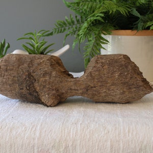 May include: A rustic wooden planter with two separate compartments, each holding a small succulent plant. The planter is made of natural wood with a rough, textured surface.