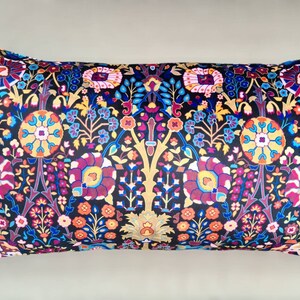 May include: A black pillow with a colorful floral pattern and black tassels. The pillow is rectangular and has a soft, plush texture.