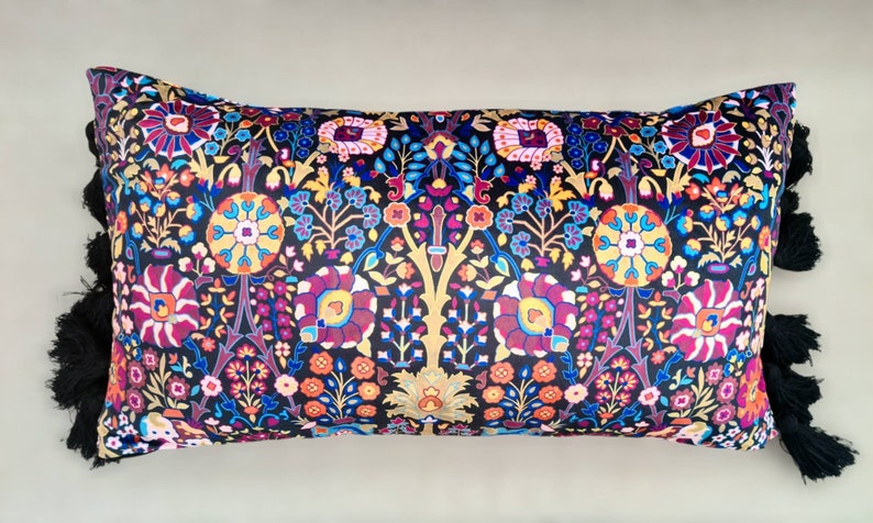 May include: A black pillow with a colorful floral pattern and black tassels. The pillow is rectangular and has a soft, plush texture.