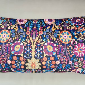 May include: A long rectangular pillow with a black background and a colorful floral pattern. The pillow has pink tassels on each end.