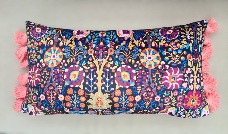 May include: A long rectangular pillow with a black background and a colorful floral pattern. The pillow has pink tassels on each end.