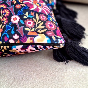 May include: A decorative throw pillow with a colorful floral pattern and black tassels. The pillow is made of a soft, plush fabric and has a zipper closure.