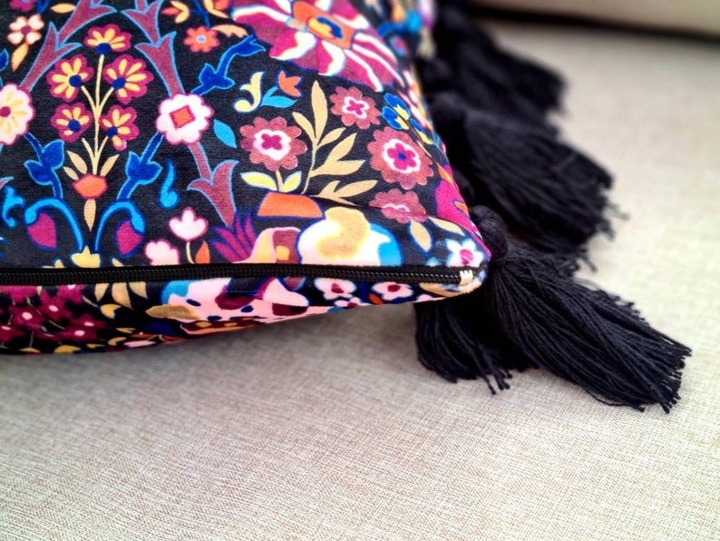 May include: A decorative throw pillow with a colorful floral pattern and black tassels. The pillow is made of a soft, plush fabric and has a zipper closure.