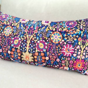 May include: A long rectangular pillow with a black background and a colorful floral pattern. The pillow has pink tassels on each end.