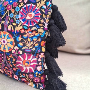 May include: A black pillow with a colorful floral pattern and black tassels on the edge.