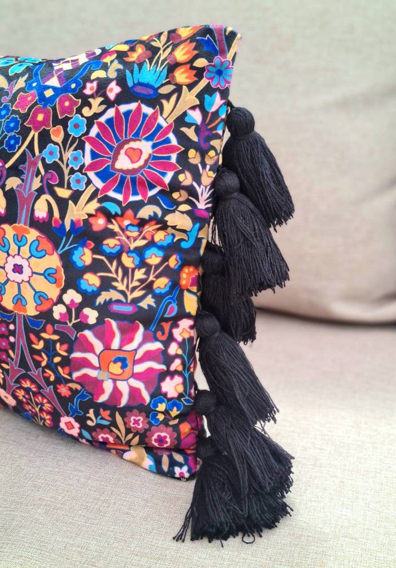 May include: A black pillow with a colorful floral pattern and black tassels on the edge.