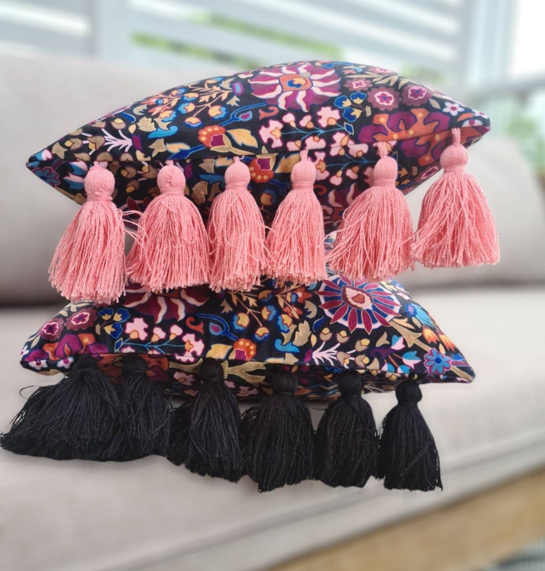 May include: Two decorative throw pillows with black and white floral patterns and tassels. The top pillow has pink tassels and the bottom pillow has black tassels.