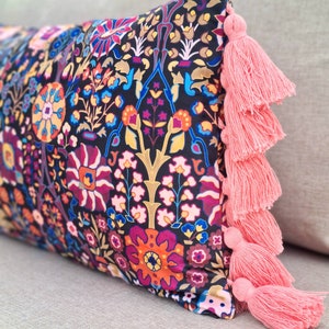 May include: A decorative pillow with a black background and a colorful floral pattern. The pillow has pink tassels on the edges.