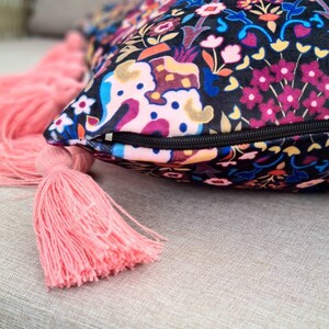 May include: A decorative throw pillow with a black background and a colorful floral pattern. The pillow has a zipper closure and pink tassels.