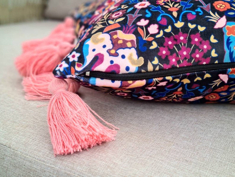 May include: A decorative throw pillow with a black background and a colorful floral pattern. The pillow has a zipper closure and pink tassels.