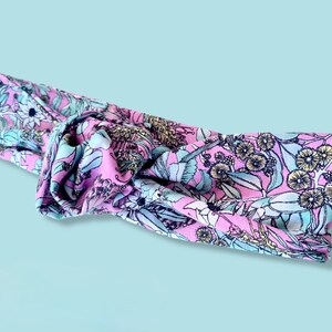 May include: A pink headband with a floral pattern featuring blue and yellow flowers. The headband is tied in a knot.