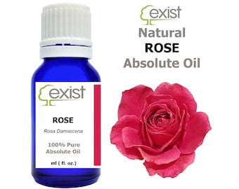 May include: A blue glass bottle with a white cap, labelled "Exist Natural Rose Absolute Oil" and "Rosa Damascena 100% Pure Absolute Oil ml (fl. oz.)". A pink rose is shown in the background.