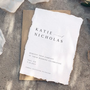 May include: A white wedding invitation with a rustic, hand-torn edge. The invitation reads "KATIE and NICHOLAS REQUEST YOUR COMPANY AT THEIR WEDDING CELEBRATION VAIL, CO 7.10.2023 FORMAL INVITATION TO FOLLOW."