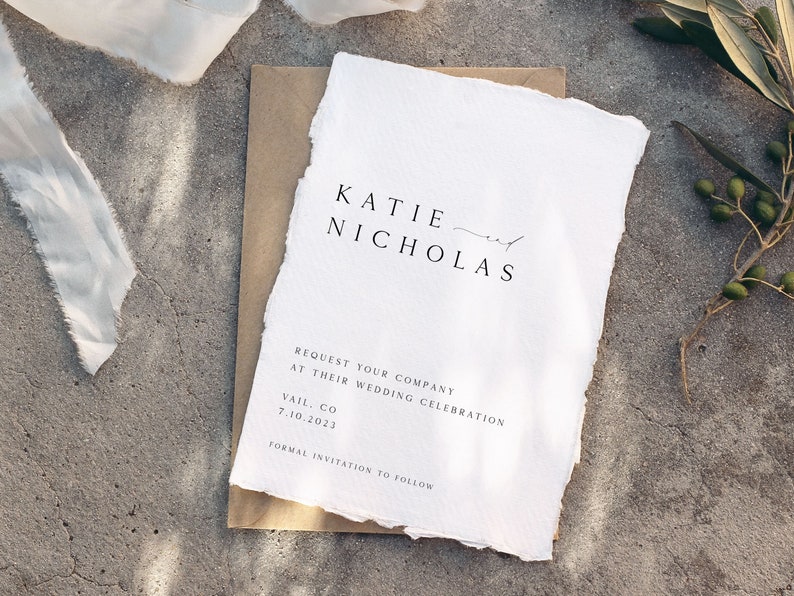 May include: A white wedding invitation with a rustic, hand-torn edge. The invitation reads "KATIE and NICHOLAS REQUEST YOUR COMPANY AT THEIR WEDDING CELEBRATION VAIL, CO 7.10.2023 FORMAL INVITATION TO FOLLOW."