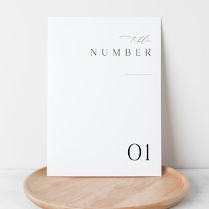 May include: White card with black text that reads "Table Number 01". The card is sitting on a wooden tray.