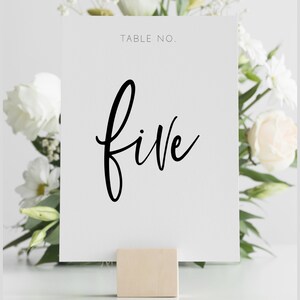 May include: White card with black calligraphy that says "TABLE NO. five" on a wooden stand.