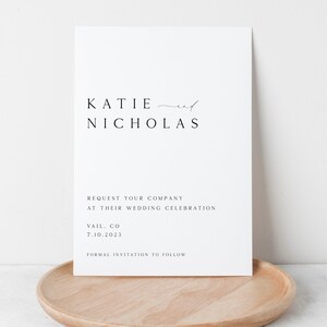 May include: A white save the date card with black text announcing the wedding of Katie and Nicholas. The card states "Request your company at their wedding celebration" and includes the date and location: Vail, CO 7.10.2023. The card also states "Formal invitation to follow."