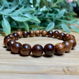 May include: A brown wooden beaded bracelet with a smooth, polished finish. The bracelet is made of round beads that are strung together on a string.
