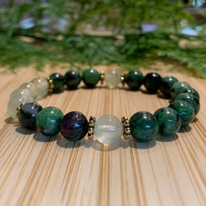 Peut inclure: Un bracelet en pierres précieuses vertes et blanches avec des accents dorés. Le bracelet est composé de perles rondes et présente une variété de pierres vertes et blanches.