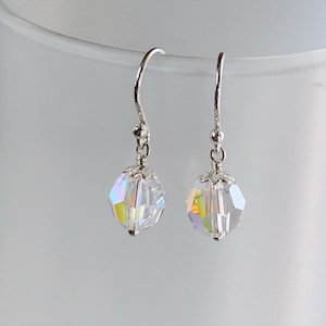 May include: A pair of clear crystal earrings with iridescent facets. The earrings have a silver-coloured hook and a small silver bead above the crystal. The crystals are faceted and catch the light, displaying a rainbow of colours.