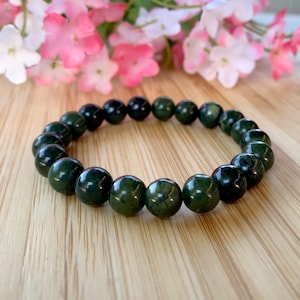 May include: A dark green jade stone bracelet with round beads. The bracelet is on a wooden surface.