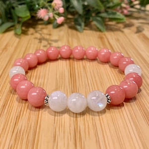 Puede incluir: Un brazalete de piedras preciosas rosa y blanco con cuentas de plata. El brazalete está hecho con cuentas redondas rosas y blancas.