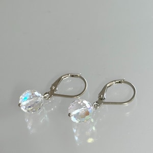 May include: A pair of clear crystal ball earrings with silver lever-back clasps. The earrings are round and faceted, reflecting light. The jewellery is displayed on a light-coloured surface.