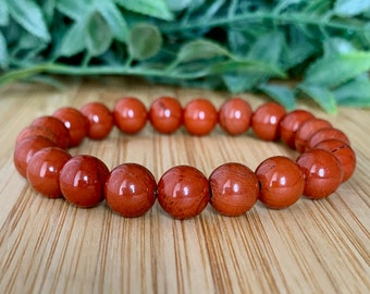 May include: A red jasper beaded bracelet with a polished finish. The bracelet is made of round beads and is strung on elastic.