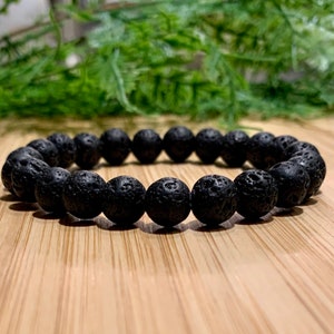 May include: A black lava rock beaded bracelet. The bracelet is made of round, black beads with a rough, textured surface.