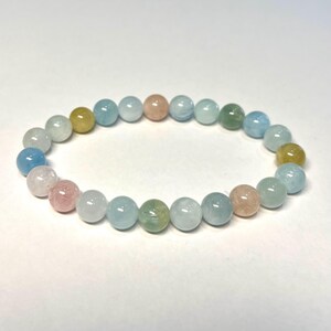May include: A bracelet made of round, multi-coloured gemstone beads. The beads are shades of blue, green, pink, and yellow.