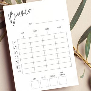 May include: A white Bunco score sheet with a handwritten-style "Bunco" title. The sheet includes spaces for name, game numbers, and score tracking. Dice icons are on the left. The sheet is surrounded by green leaves.