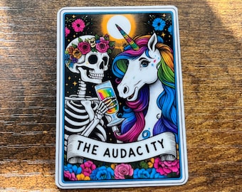 May include: A rectangular sticker featuring a skeleton and a unicorn. The skeleton wears a floral crown and holds a rainbow-colored drink. The unicorn has a rainbow mane and horn. The text "THE AUDACITY" is on a banner below.