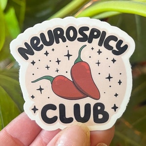May include: A pink and white sticker with the text "Neurospicy Club" in black lettering. Two red chilli peppers are illustrated in the centre of the sticker.